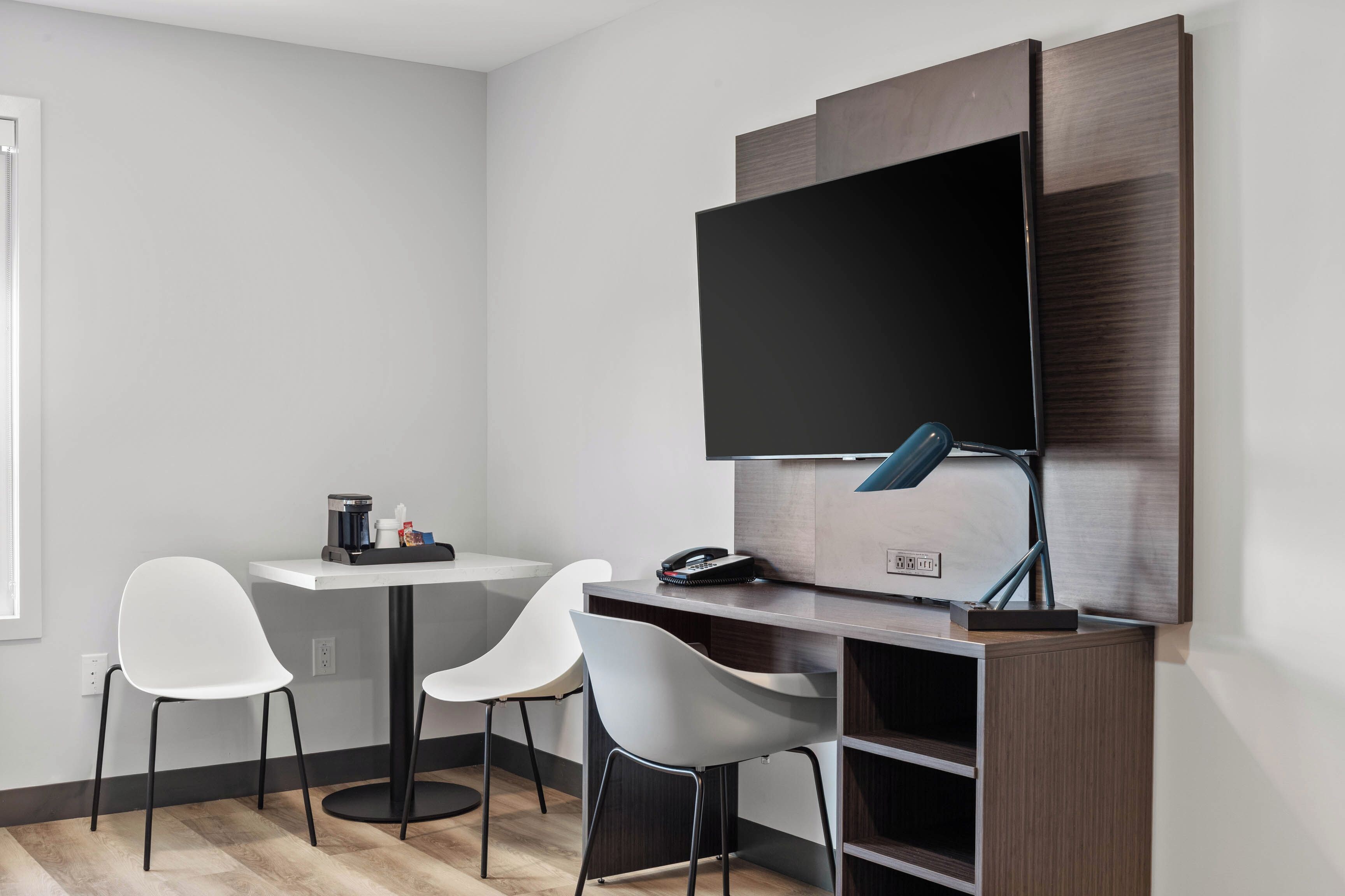 Un espace de bureau moderne comprenant un bureau, deux chaises, un téléviseur à écran plat et une lampe de bureau.