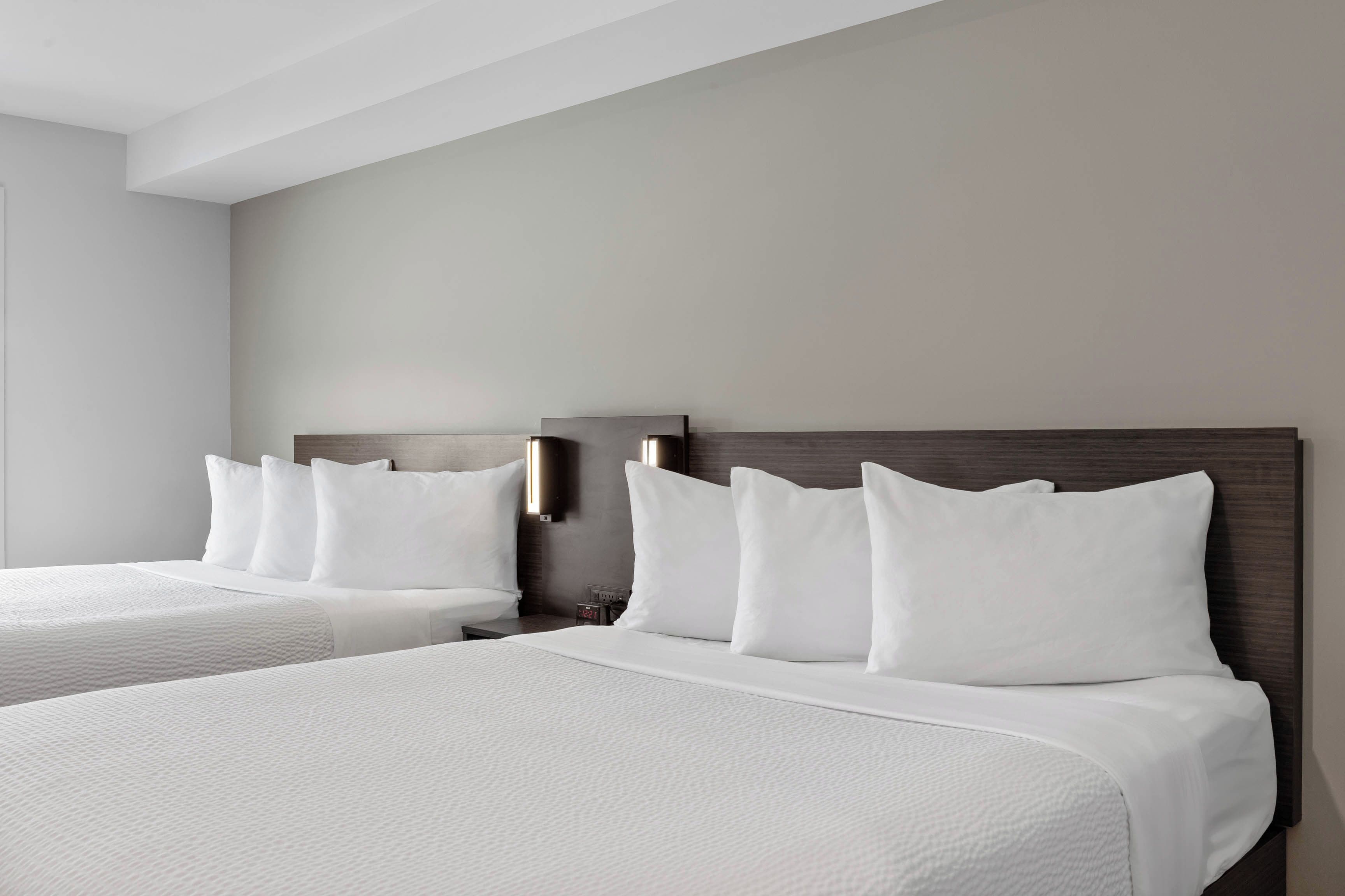 Ein Hotelzimmer mit zwei Betten, jeweils mit weißer Bettwäsche und Kissen, einem hölzernen Kopfteil und einem Nachttisch mit einer Uhr.