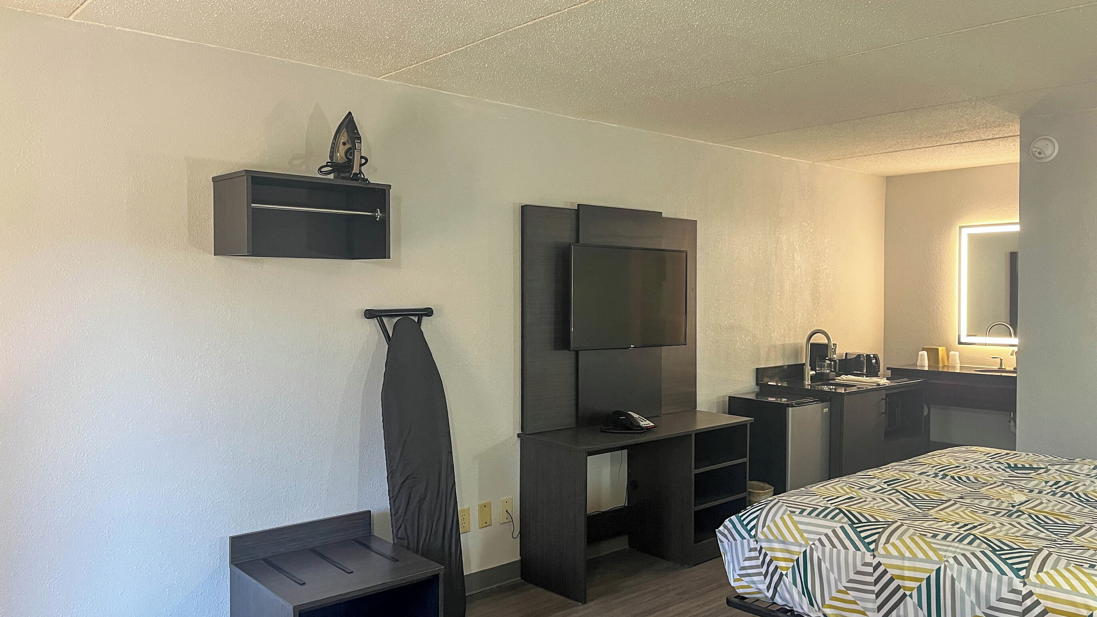 A hotel room with a bed, a TV, a desk, a mirror, and a small iron.