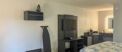A hotel room with a bed, a TV, a desk, a mirror, and a small iron.