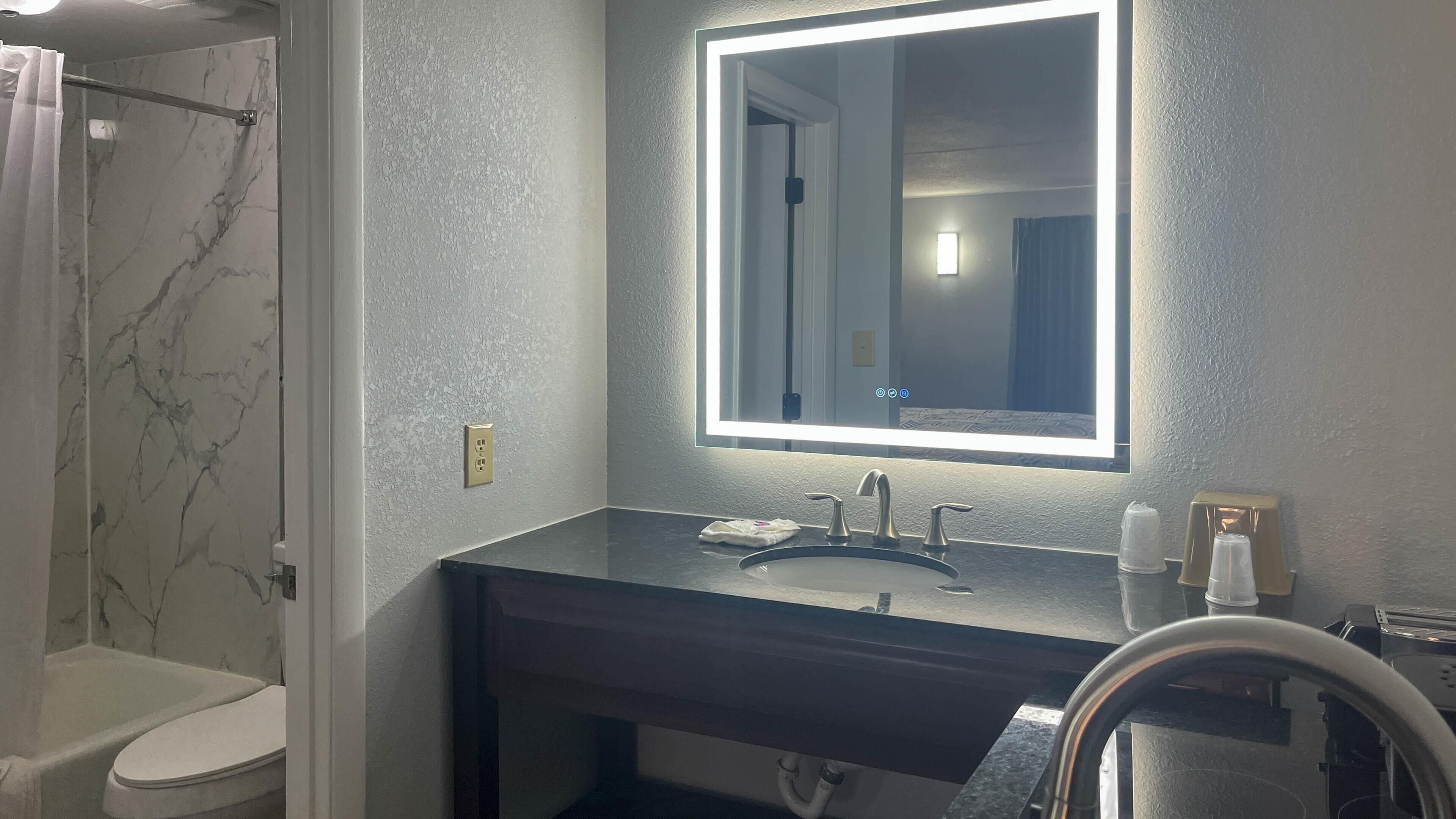 A bathroom with a marble shower, a sink with a mirror, and a toilet.