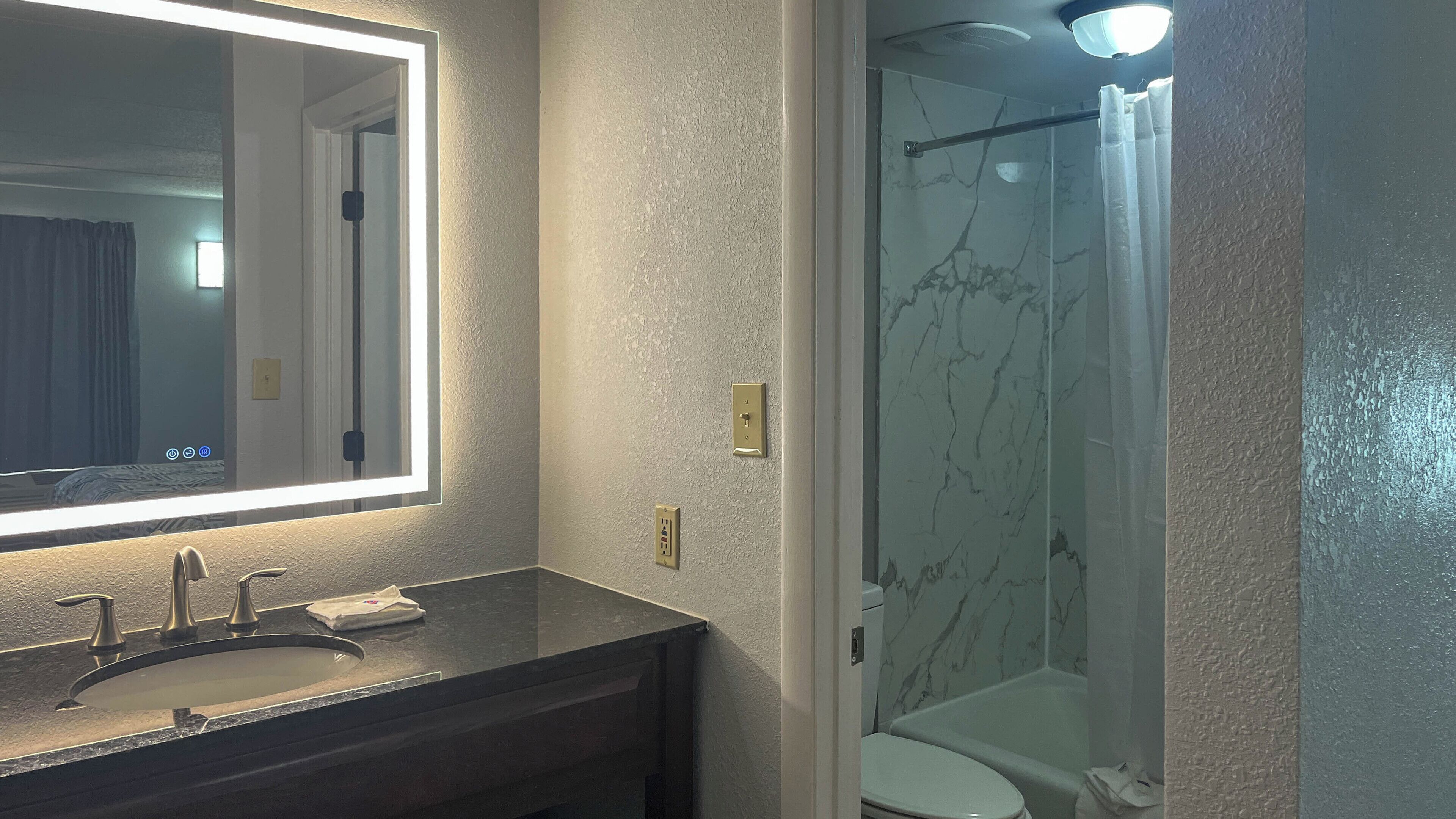 A bathroom with a large mirror, a sink, a toilet, and a shower.