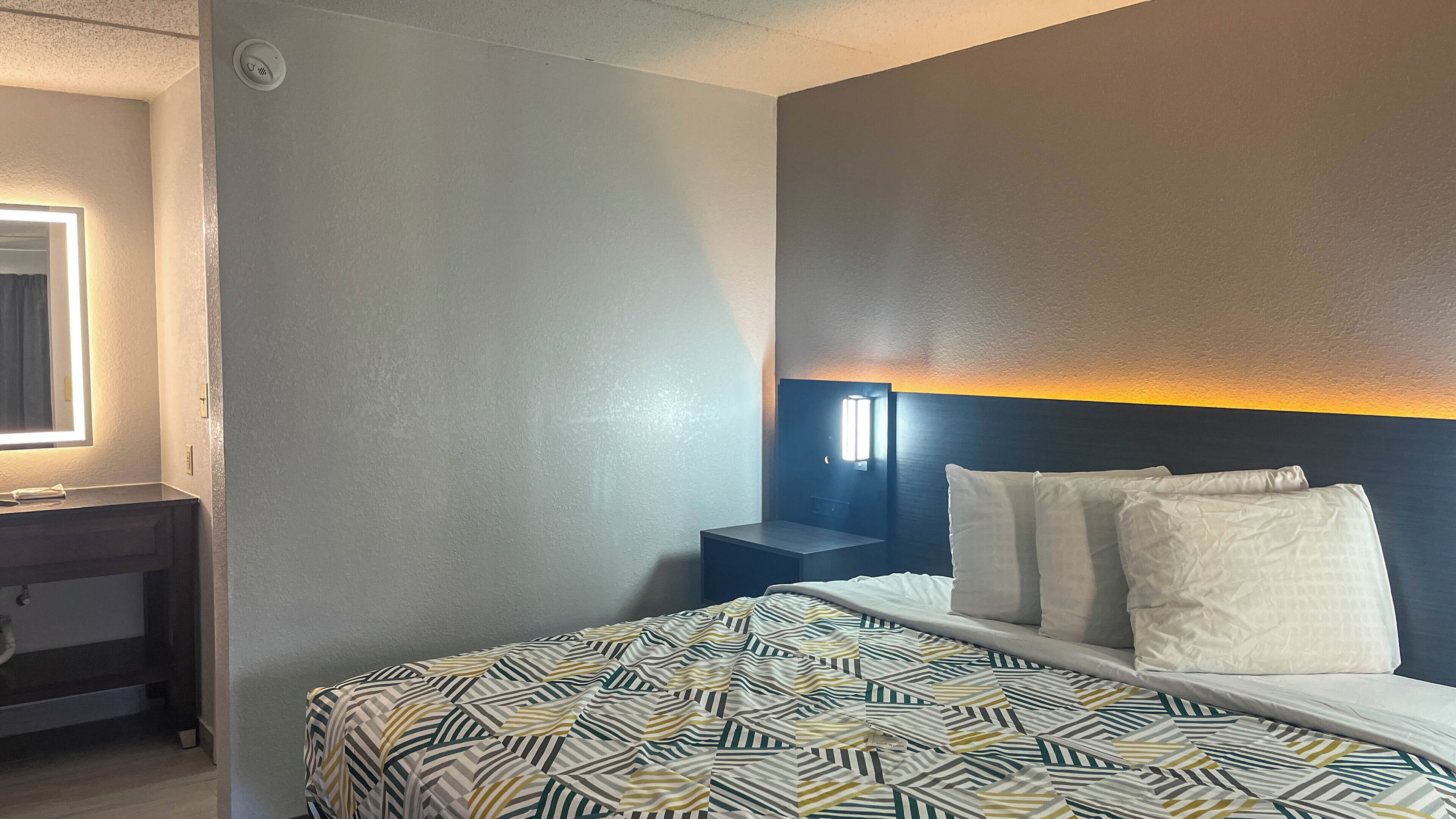 A hotel room with a bed, bedside table, and a wall-mounted light fixture.