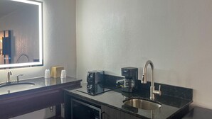 Un bagno moderno con un piano d'appoggio scuro, un lavabo, uno specchio, una macchina del caffè e una lavastoviglie.