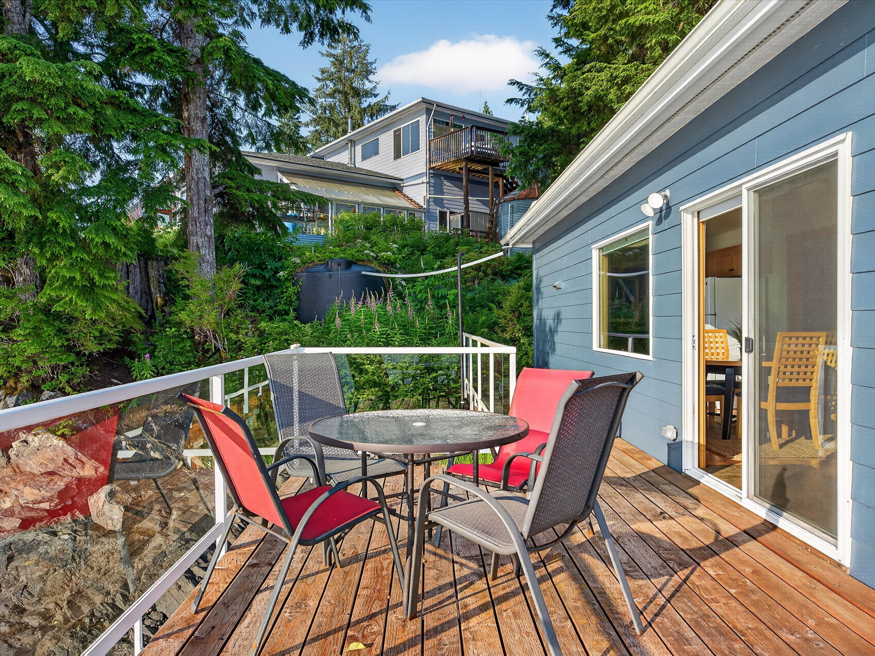 A deck with a table and chairs, overlooking a forested area and a building with a balcony.
