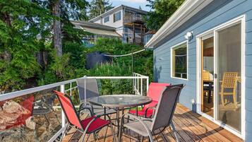 A deck with a table and chairs, overlooking a forested area and a building with a balcony.