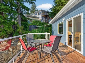 Une terrasse avec une table et des chaises, donnant sur une zone boisée et un bâtiment doté d’un balcon.