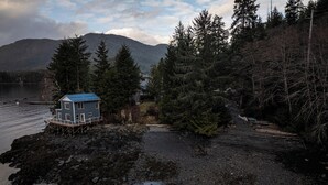 Uma casa sobre pilares junto a um lago, com uma floresta ao fundo.