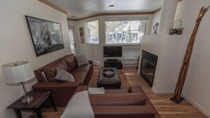 A living room with a brown leather sofa, a small table with a lamp, a flat-screen TV, and a fireplace. - Cozy 1-bedroom condo seconds from bus line in East Vail, perfect for getaways. (Vail)