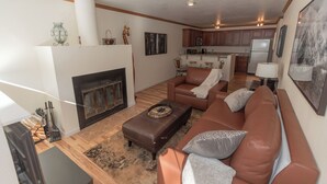 A living room with a fireplace, leather sofa, and a dining area with wooden cabinets and a refrigerator. - Cozy 1-bedroom condo seconds from bus line in East Vail, perfect for getaways. (Vail)