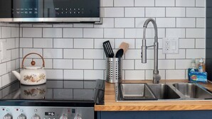 A kitchen with a stove, oven, and sink. There is a kettle on the stove, a set of utensils in a holder, and a bottle of dish soap on the counter. - Bay View A-Frame + King Bed | 5-Min Walk to Beach (Blaine)