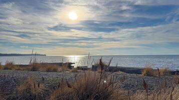 A beach with a rocky foreground and a calm sea under a partly cloudy sky.
