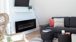 A modern living room with a fireplace, a sofa, a coffee table, and a TV mounted on the wall. - Bay View A-Frame + King Bed | 5-Min Walk to Beach (Blaine)