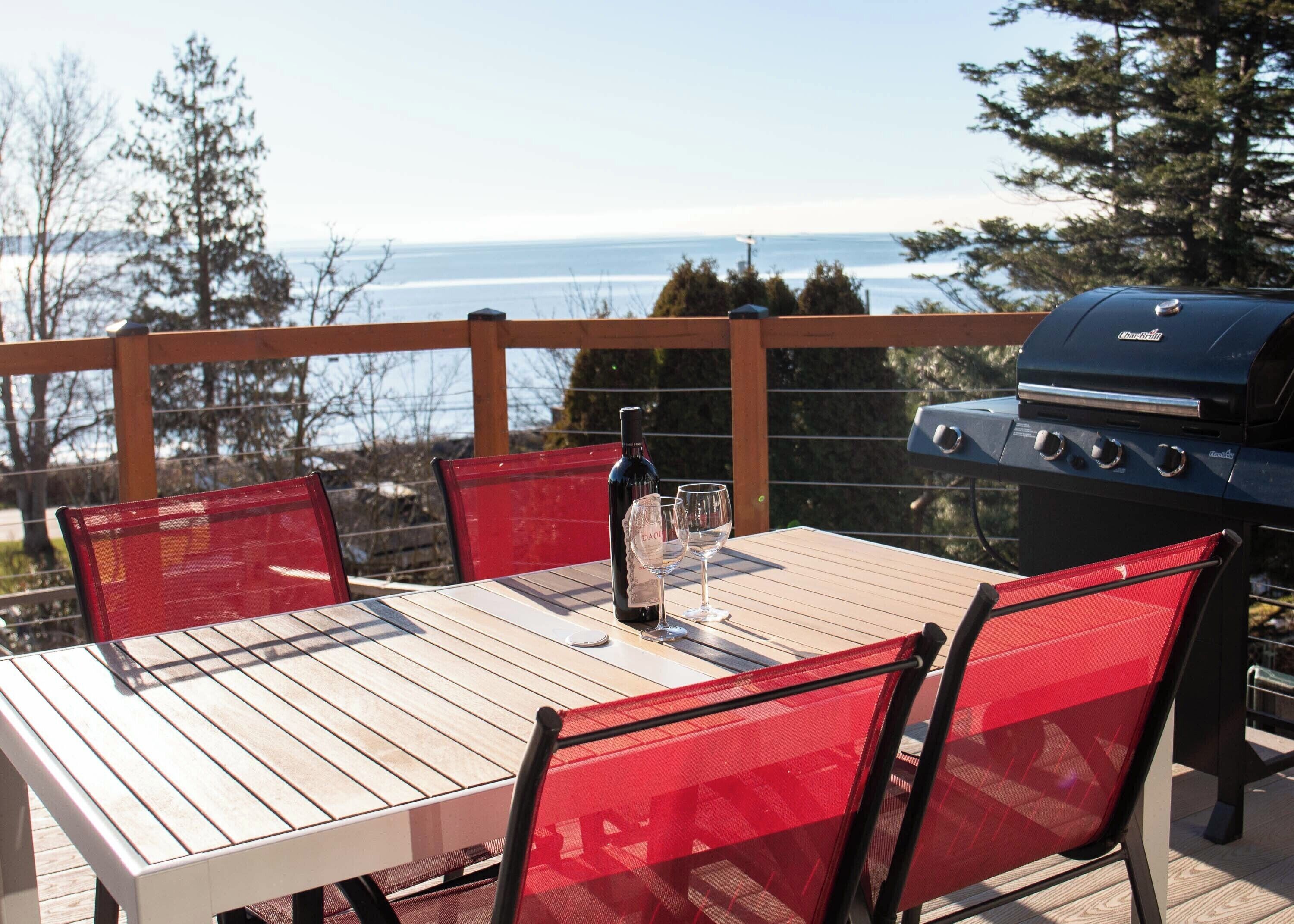 An outdoor patio with a table and chairs, a grill, and a view of the ocean.