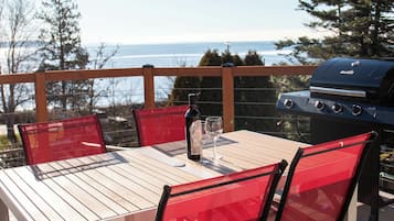 An outdoor patio with a table and chairs, a grill, and a view of the ocean.