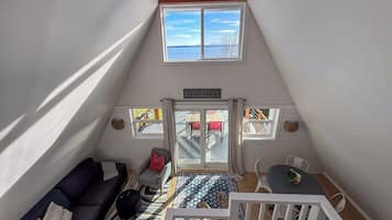A cozy loft bedroom with a sloped ceiling, a ceiling fan, a large skylight, a view of the outdoors, a bed, a nightstand, and a window with a view of the beach.