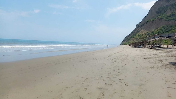 A beach with a sandy shore, a few footprints, and a structure with a roof on the right side.