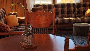 Une pièce chaleureuse avec un plafond en bois, un lustre, un canapé, une table à manger avec des chaises et une fenêtre avec des rideaux.