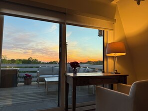 A room with a large window, a table with a lamp, a chair, and a sofa.
