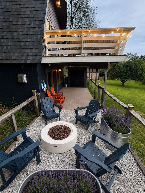 A covered outdoor seating area with Adirondack chairs, a fire pit, and potted lavender plants.