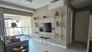 Een moderne woonkamer met een flatscreen televisie, een bank, een salontafel en een balkon met uitzicht op gebouwen.