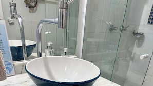 Un baño con un lavabo azul grande, un lavamanos blanco y una cabina de ducha de vidrio.