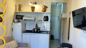 Cocina compacta con armarios blancos, microondas, cafetera y pileta. En la zona de estar contigua, hay un sofá y una mesa de comedor con sillas.
