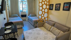 Habitación de hotel con dos camas, un sofá, una mesa de comedor con sillas y un separador decorativo.