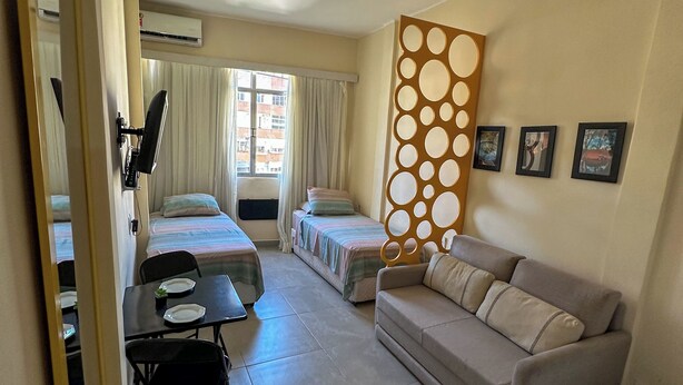 Habitación de hotel con dos camas individuales, un sofá, una mesa de comedor con sillas y un panel decorativo con círculos recortados.