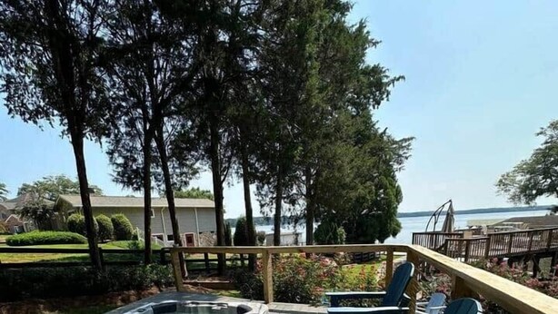 Eine Holzterrasse mit Whirlpool und Liegestühlen, die auf ein Gewässer ausgerichtet ist.