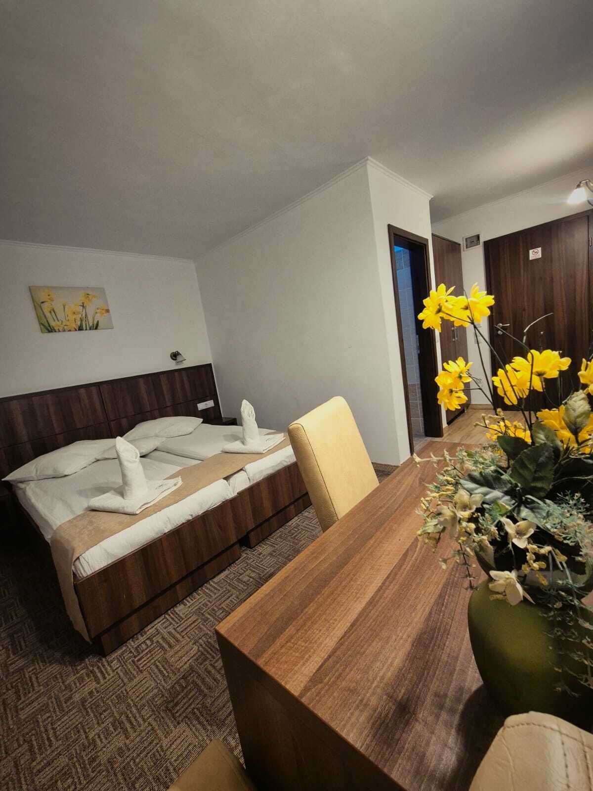 Una camera d'albergo con un letto di legno, un tavolo da pranzo e un vaso di fiori gialli.