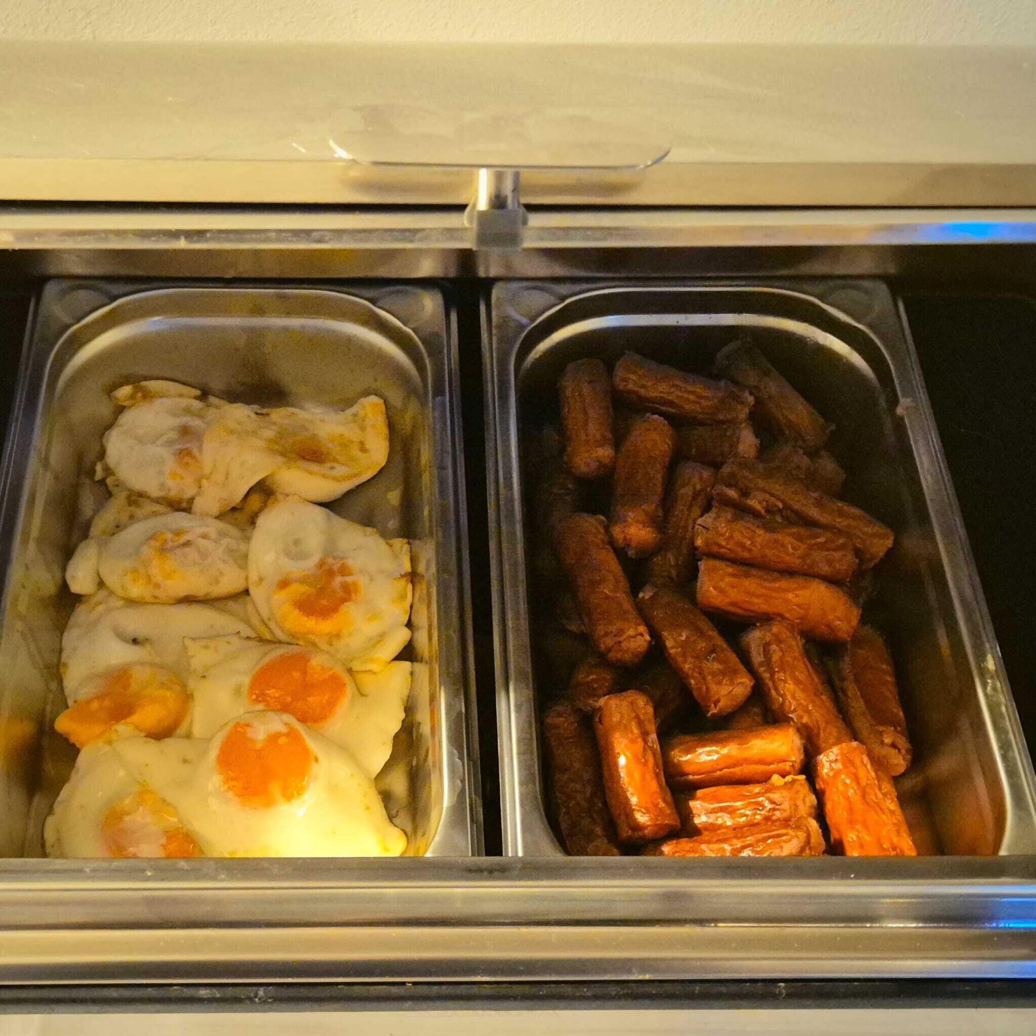 A buffet with two trays of food: one with eggs and another with sausages.