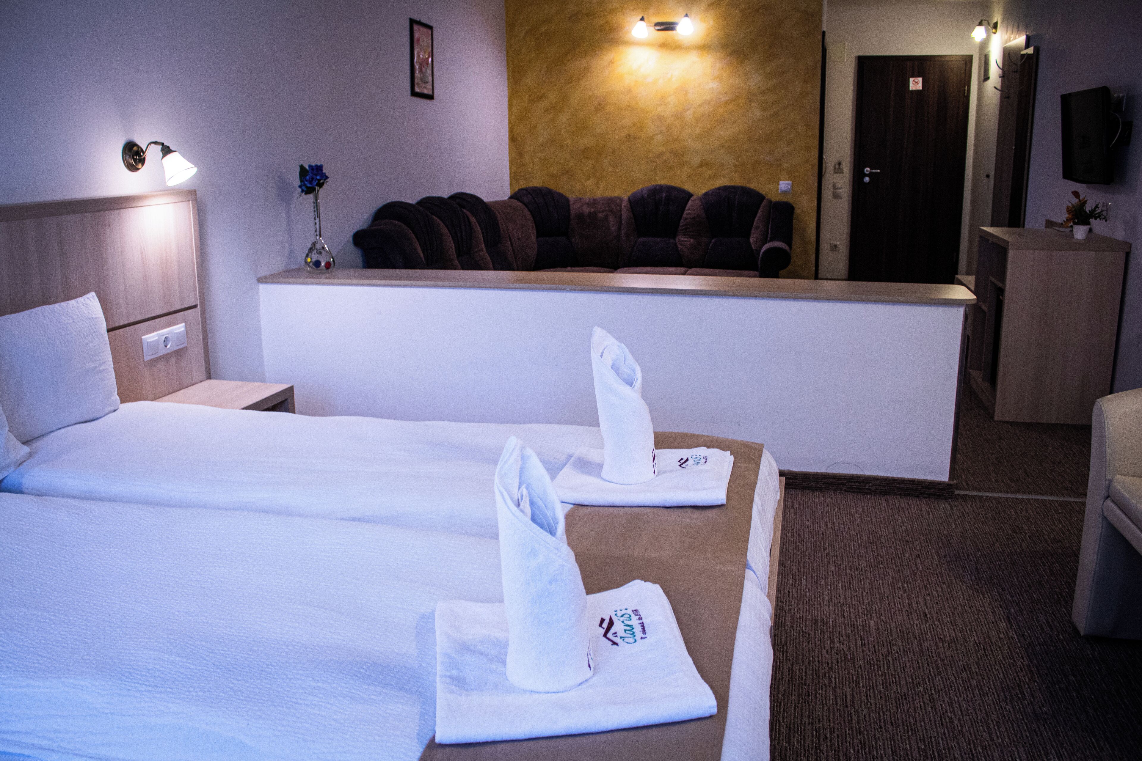 A hotel room with two beds, a reception desk, a television, and a small plant.