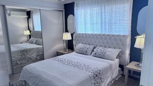 Un dormitorio con una cama grande, dos mesitas de noche, un ventilador de techo y una ventana con cortinas estampadas.
