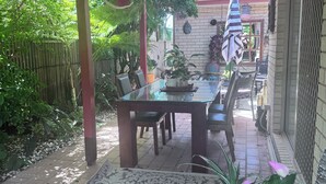 Un patio cubierto con una mesa y sillas para comer, rodeado de plantas en macetas y un paraguas decorativo.