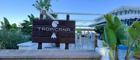 Et træskilt med navnet "TROP/CANA" og en svane-logo, der angiver et hotel eller resort.