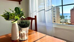 A wooden table with a potted plant, a candle, and a window with a view of buildings and the ocean. - Carihuela Beach studio, 2nd line of the beach (Torremolinos)
