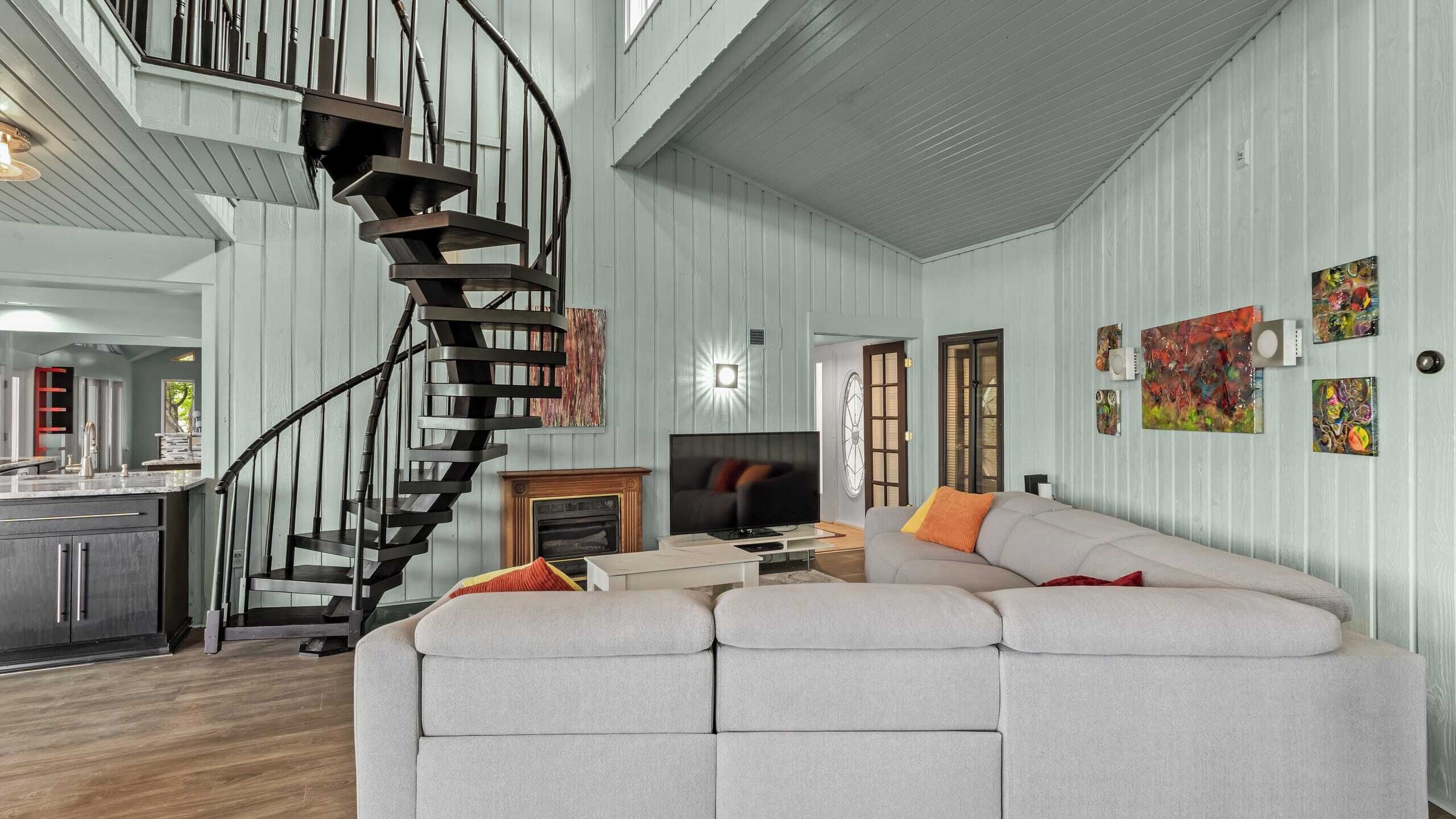 A spacious living room with a curved staircase, a large sofa, a television, and a fireplace.