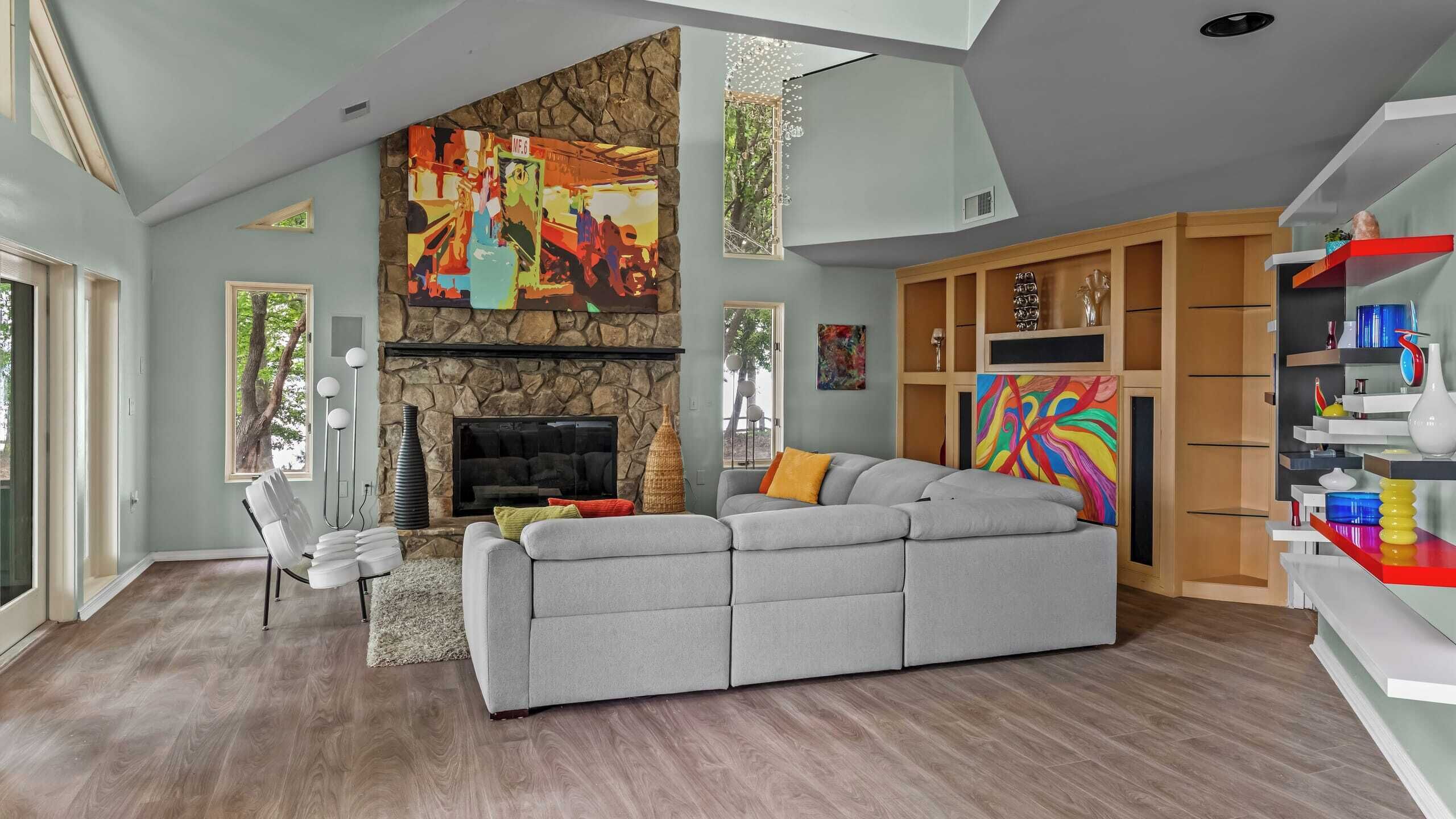 Ein modernes Wohnzimmer mit Kamin aus Stein, einem grauen Ecksofa und einem farbenfrohen, abstrakten Gemälde darüber.