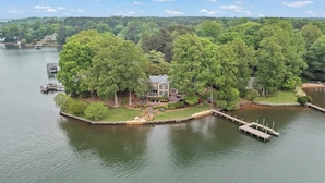 A lakeside property with a large house surrounded by dense trees, docked boats, and a well-maintained garden. - Waterfront Stay w/ Canoes, Deck, Game Room & Lake Views Near Mooresville Renwick Cove by Avantstay (Mooresville)