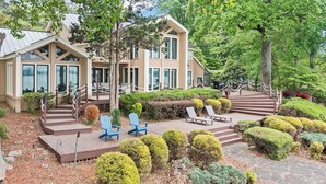 A modern building with a wooden facade, multiple windows, and a landscaped garden with trimmed bushes and a wooden deck with chairs. - Waterfront Stay w/ Canoes, Deck, Game Room & Lake Views Near Mooresville Renwick Cove by Avantstay (Mooresville)