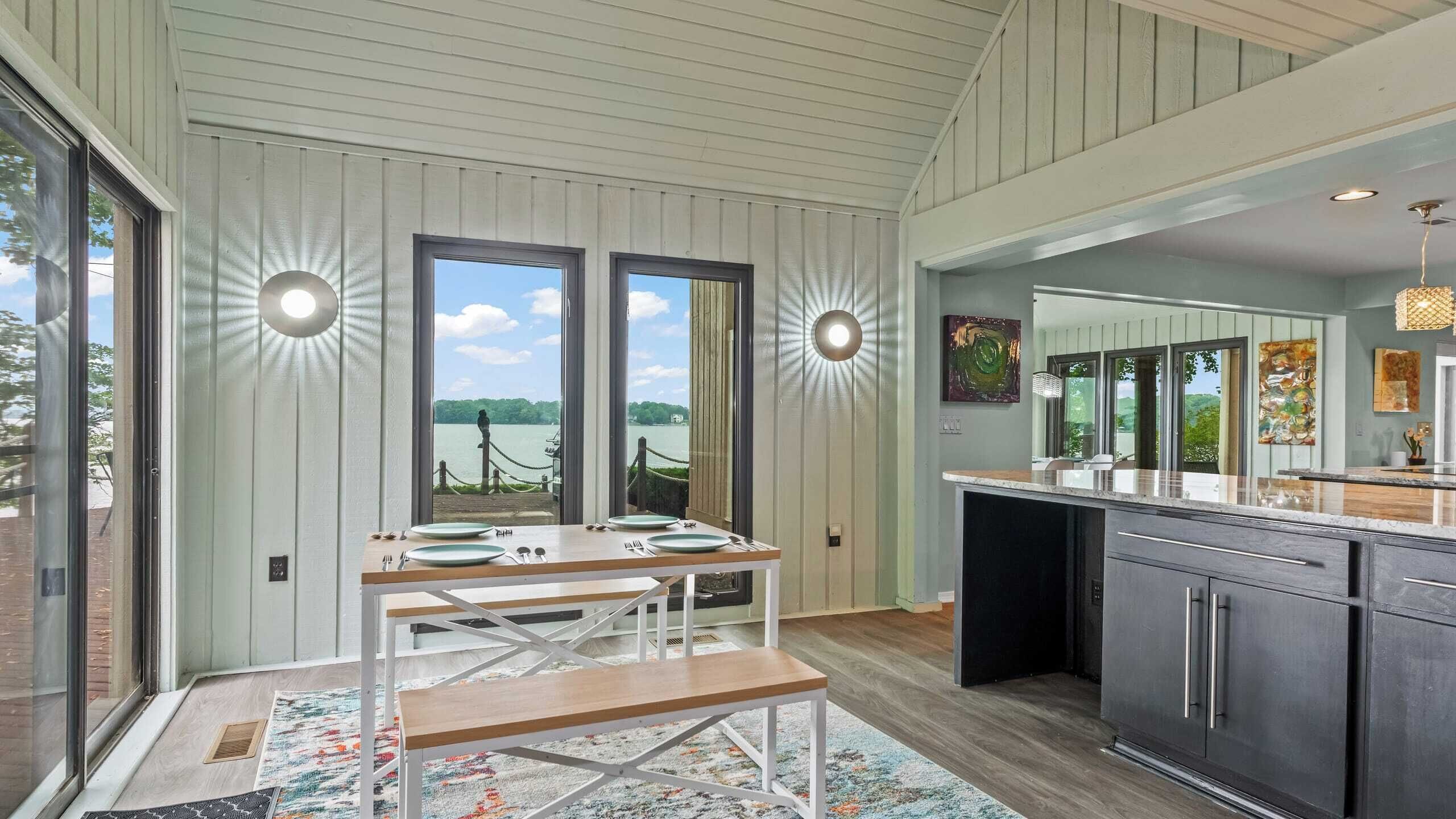 A modern kitchen with a large island, a dining area with a bench, and a view of a lake through large windows.