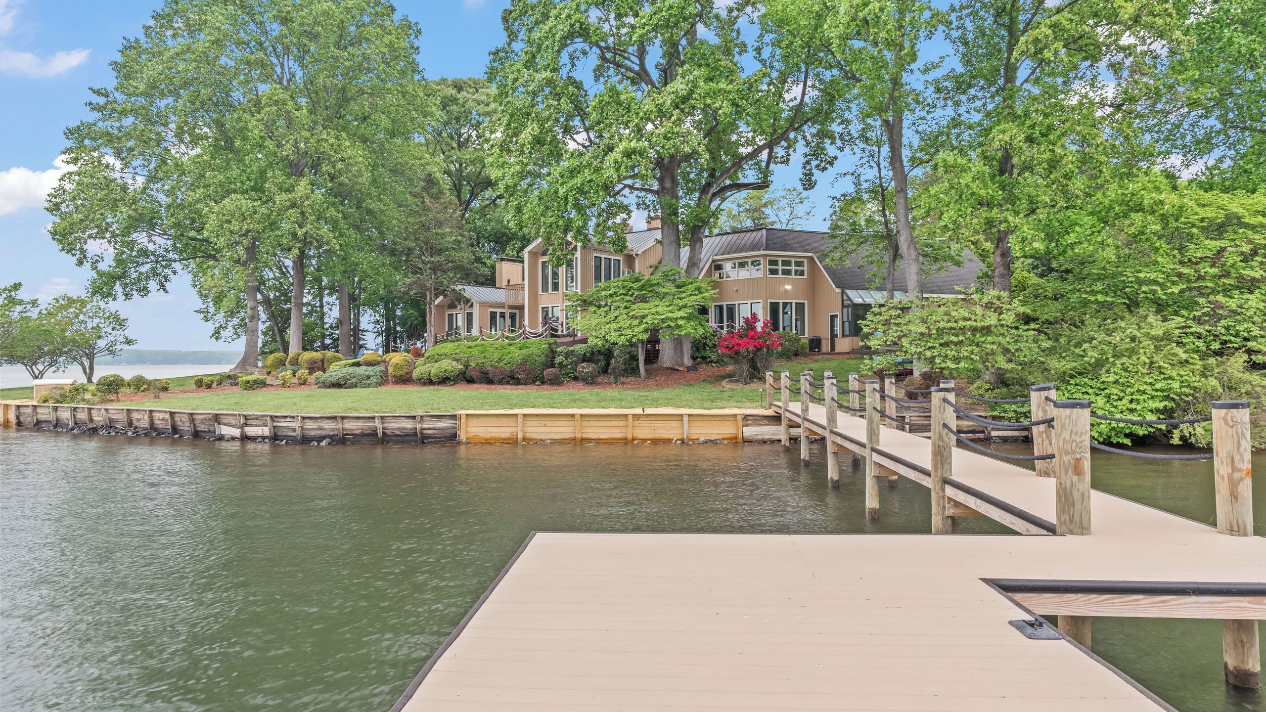 A waterfront property with a dock, a large house with multiple windows, and lush greenery.