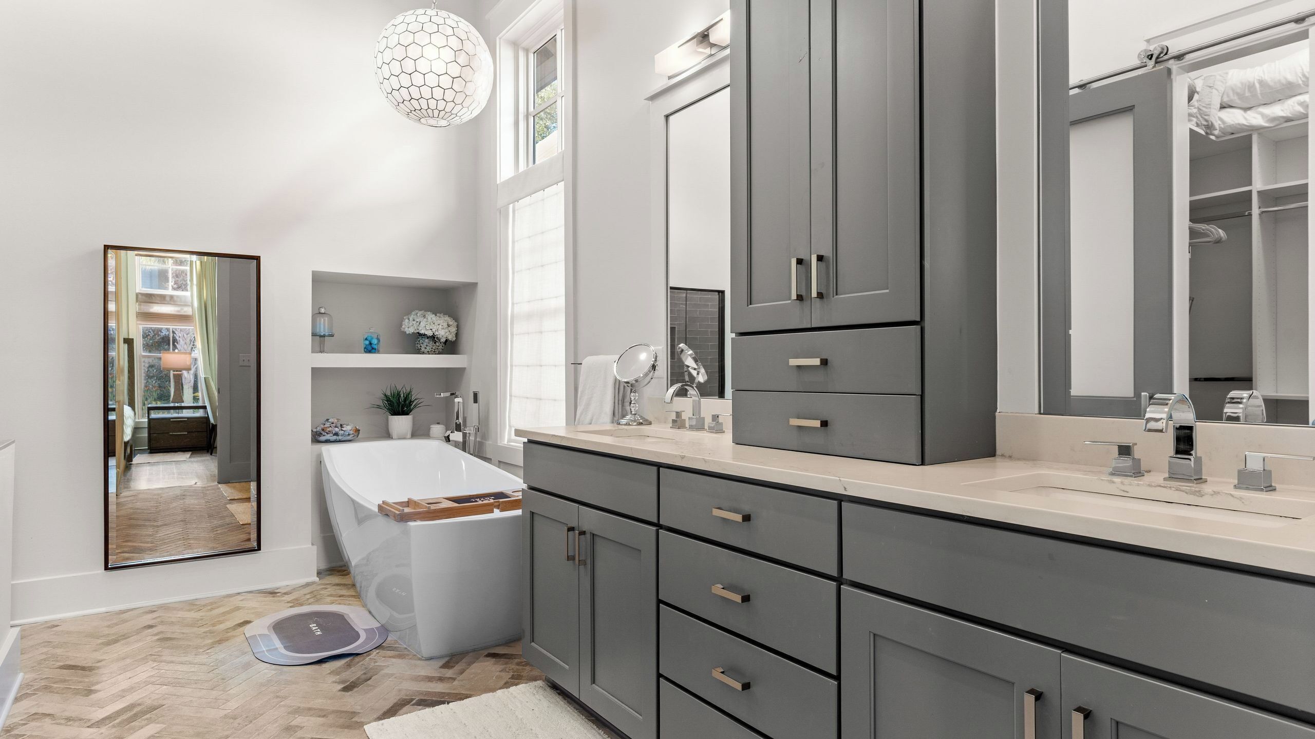 A modern bathroom with grey cabinets, a large mirror, and a bathtub.