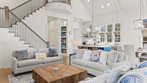 A spacious living room with a staircase, a kitchen with large windows, and a dining area. - 30A Retreat Near Gulf Place w/ Pool Access, Hammock, Bikes to Rent Always Be Summer by Avantstay (Santa Rosa Beach)