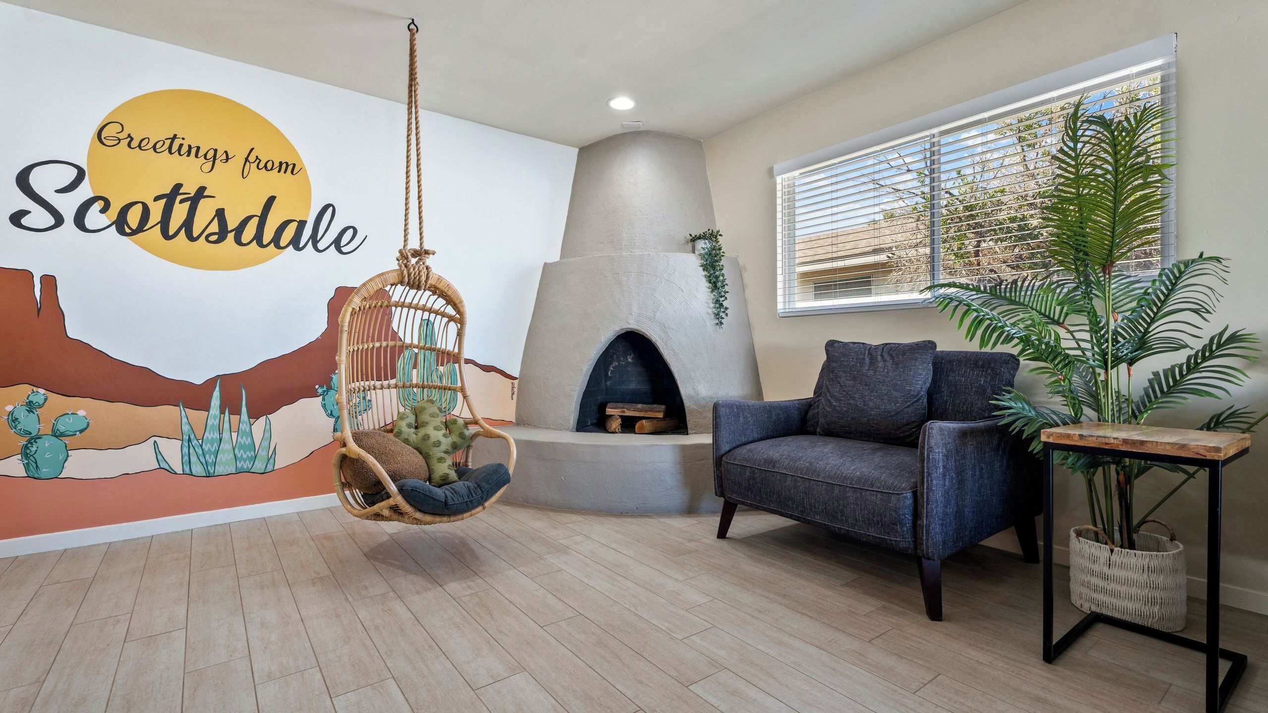 A living room with a hanging chair, a sofa, a wall mural, a fireplace, and a window with blinds.