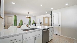 A modern kitchen with a central island, white cabinetry, and a built-in dishwasher. - Heated Pool, Fire Pit, Games & Outdoor Dining Just Minutes to Old Town Drift House by Avantstay (Scottsdale)