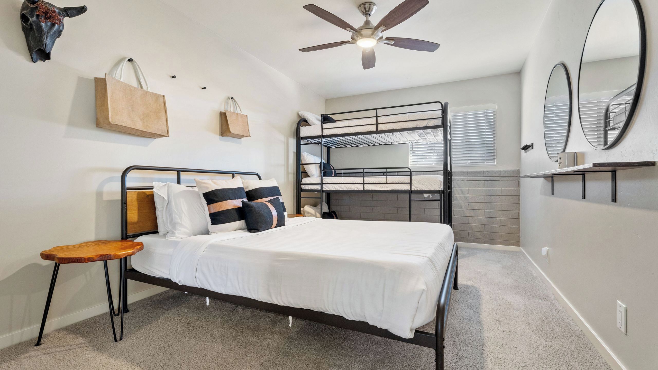 A bunk bed room with a ceiling fan, a bedside table, and a mirror on the wall.