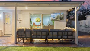 An outdoor seating area with a covered patio, a glass door entrance, and a wall with a 'Scottsdale' sign. - Heated Pool, Fire Pit, Games & Outdoor Dining Just Minutes to Old Town Drift House by Avantstay (Scottsdale)
