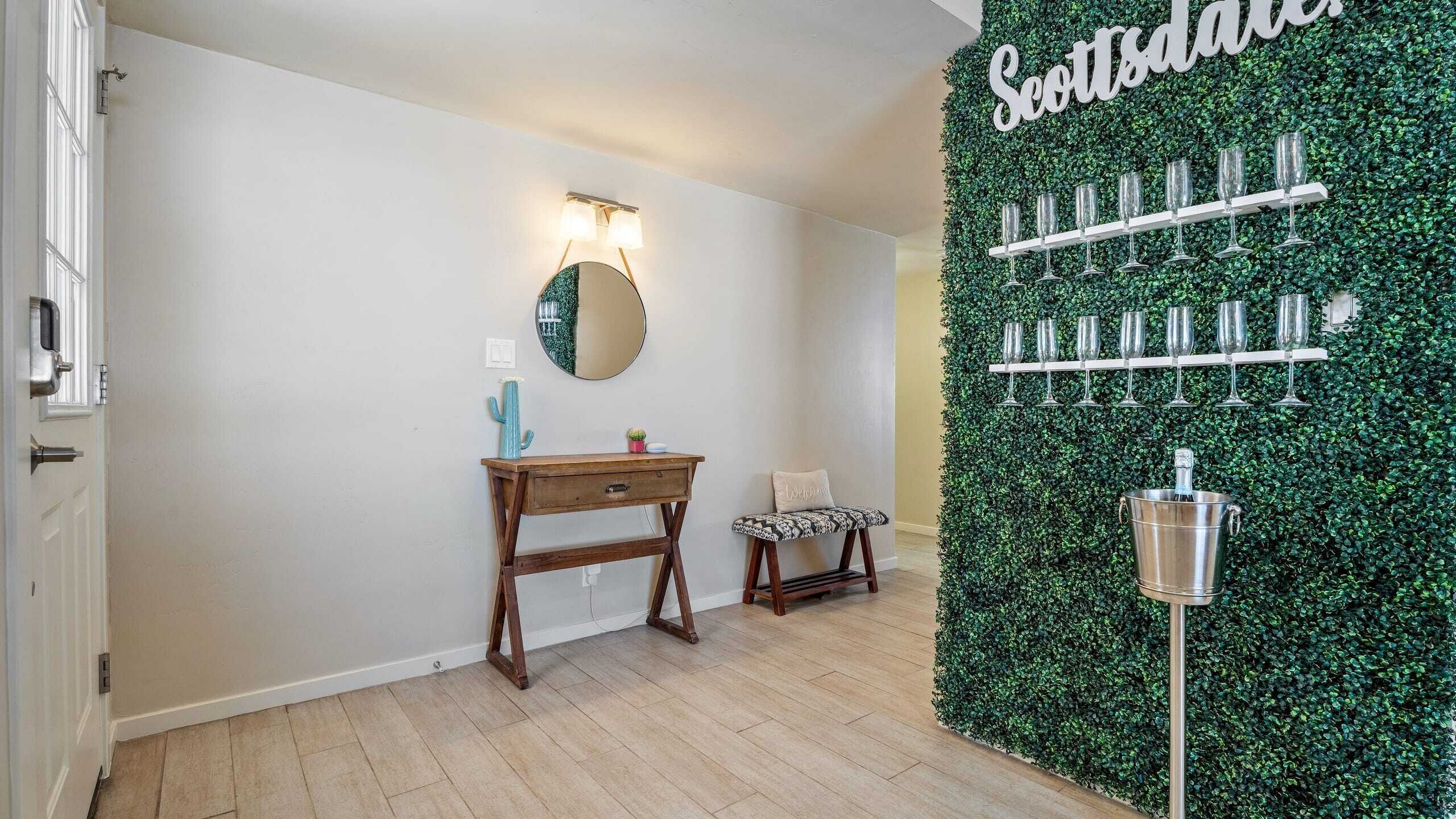 Ein Zimmer mit einer hölzernen Bank, einem kleinen Tisch, einem Spiegel und einer grünen Wand mit einem Namensschild.